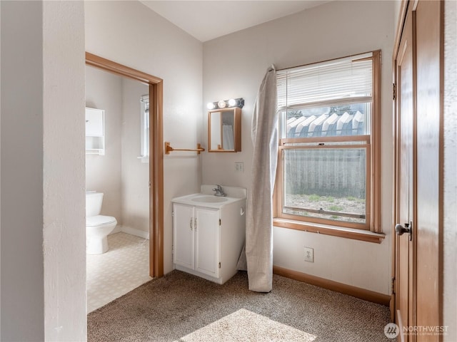 bathroom with toilet, vanity, baseboards, and a healthy amount of sunlight