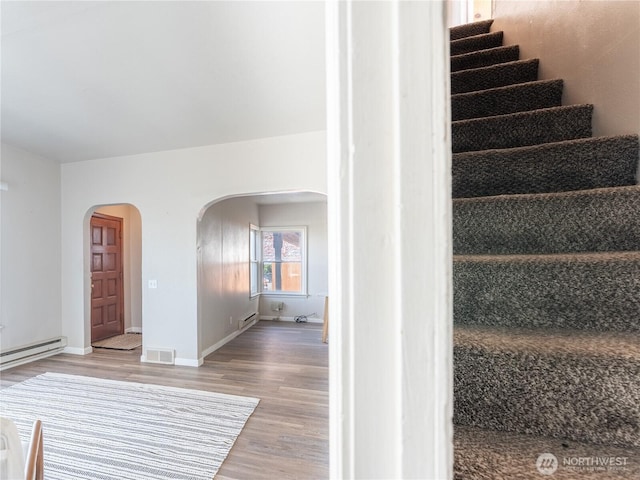 stairway with a baseboard heating unit, baseboard heating, arched walkways, visible vents, and wood finished floors