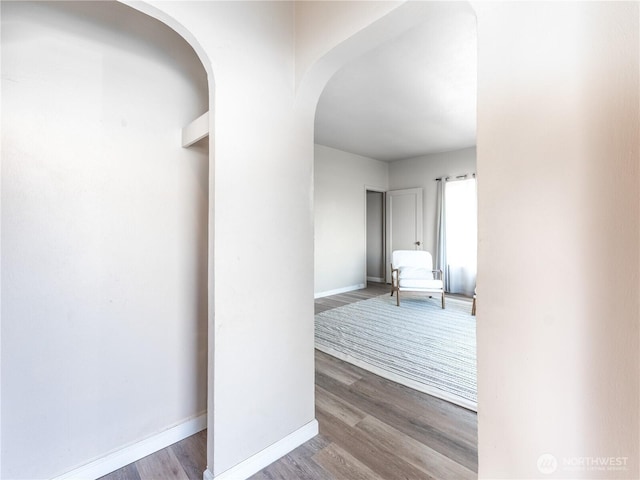 hallway featuring arched walkways, baseboards, and wood finished floors