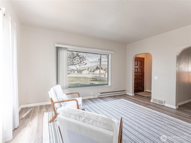 living area with arched walkways, visible vents, wood finished floors, and a baseboard radiator
