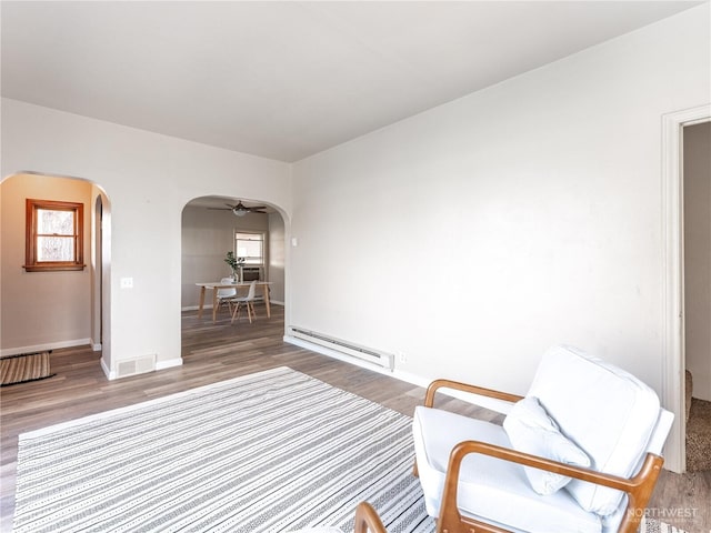 unfurnished room with arched walkways, visible vents, a baseboard heating unit, and wood finished floors