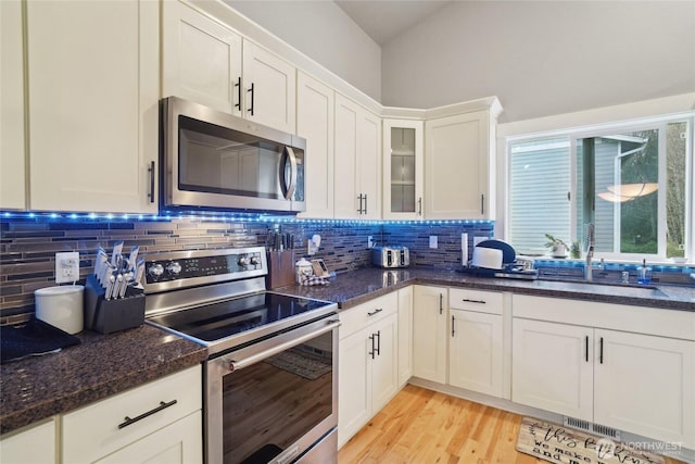 kitchen featuring decorative backsplash, stainless steel appliances, white cabinetry, a sink, and light wood-style floors