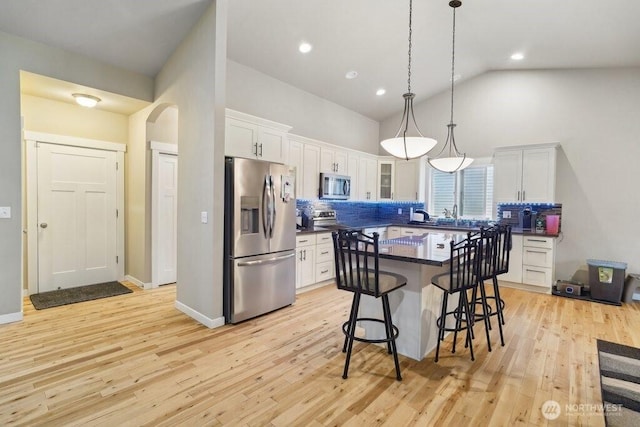 kitchen featuring high vaulted ceiling, a kitchen breakfast bar, stainless steel appliances, dark countertops, and white cabinets