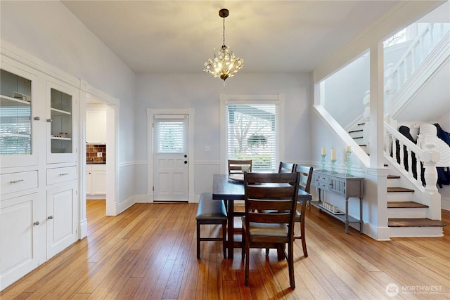 dining room featuring stairs, light wood-style flooring, and an inviting chandelier