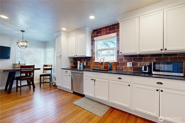 kitchen with tasteful backsplash, white cabinets, light wood-style floors, stainless steel appliances, and a sink