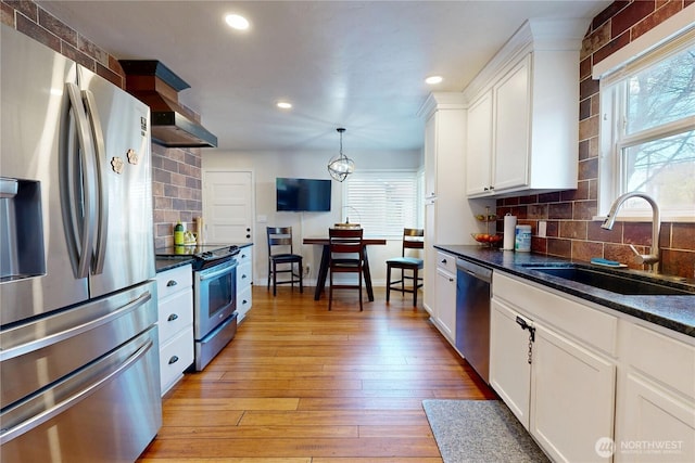 kitchen with a sink, a wealth of natural light, light wood finished floors, white cabinetry, and stainless steel appliances