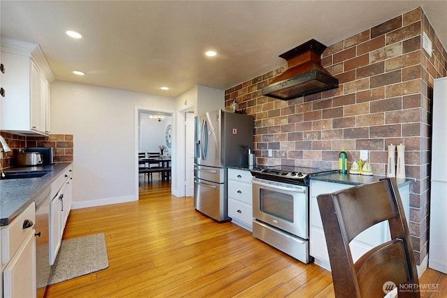 kitchen featuring custom exhaust hood, light wood-type flooring, white cabinetry, appliances with stainless steel finishes, and a sink