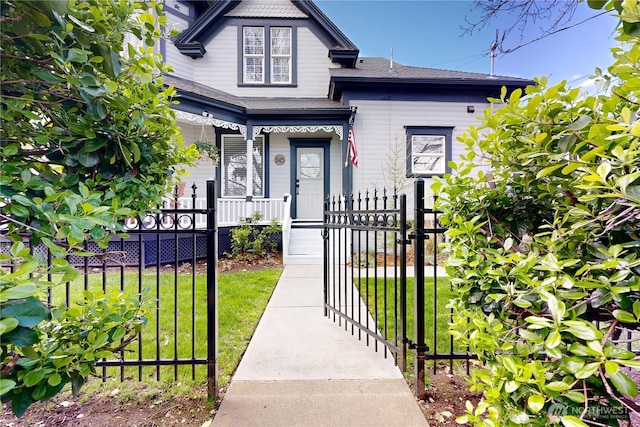 victorian-style house featuring a porch, a gate, a front lawn, and a fenced front yard
