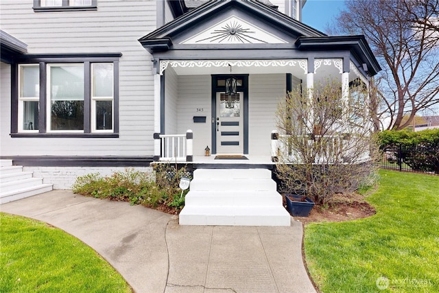 view of exterior entry featuring a yard, a porch, and fence