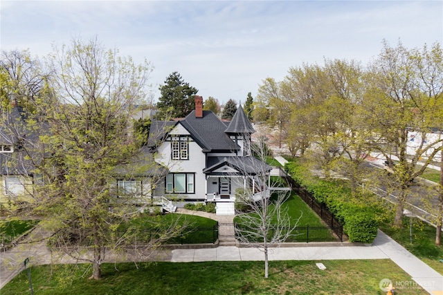 victorian home featuring a front yard, a chimney, a shingled roof, and a fenced front yard