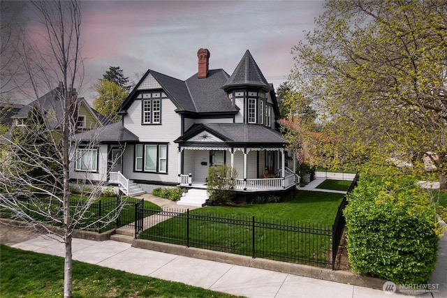 victorian-style house featuring roof with shingles, a chimney, a fenced front yard, and a front lawn