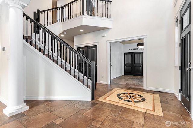 entrance foyer featuring stone tile flooring, a high ceiling, ornate columns, baseboards, and stairs