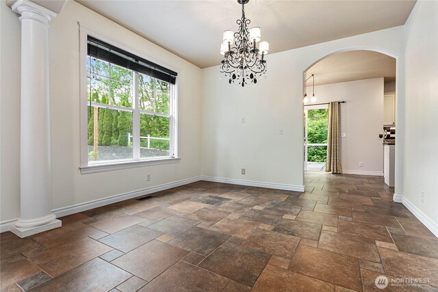 spare room featuring arched walkways, stone tile flooring, baseboards, and a chandelier