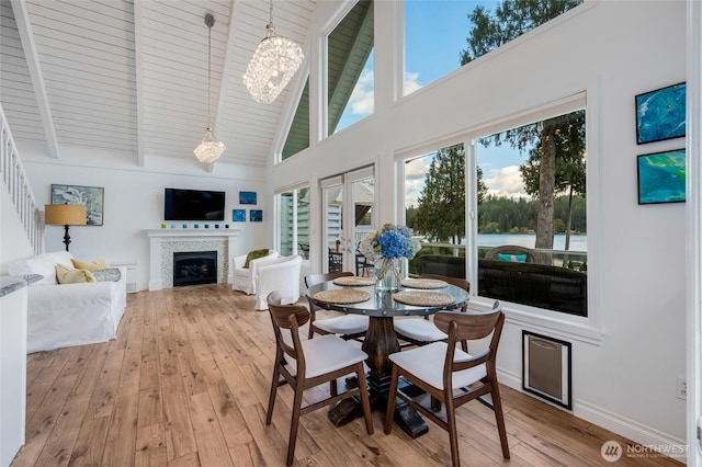 dining area with high vaulted ceiling, a chandelier, light wood-type flooring, beamed ceiling, and a fireplace