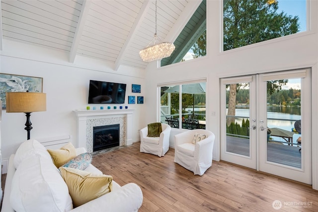 living area with high vaulted ceiling, light wood-type flooring, a fireplace with flush hearth, french doors, and beamed ceiling