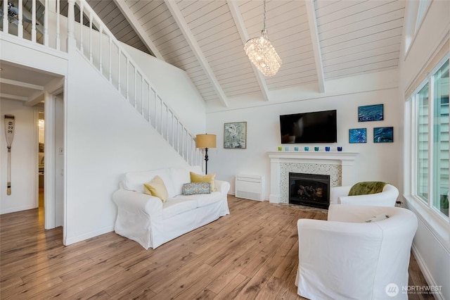 living area featuring stairway, wood finished floors, a chandelier, a fireplace, and beam ceiling