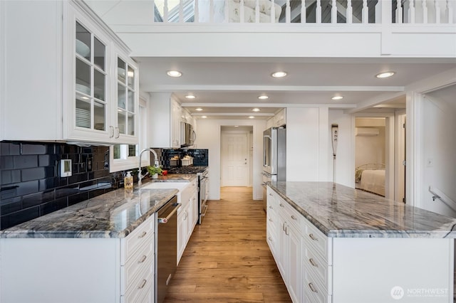 kitchen featuring white cabinets, stainless steel appliances, light wood-style floors, glass insert cabinets, and tasteful backsplash