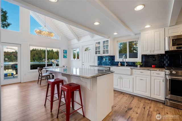 kitchen featuring a sink, decorative backsplash, stainless steel appliances, a kitchen bar, and beam ceiling
