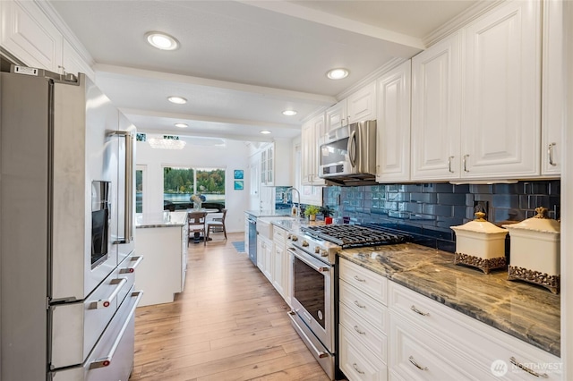 kitchen with stainless steel appliances, stone counters, light wood-style floors, white cabinetry, and decorative backsplash