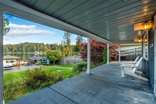 view of patio / terrace featuring grilling area, fence, a water view, and a view of trees