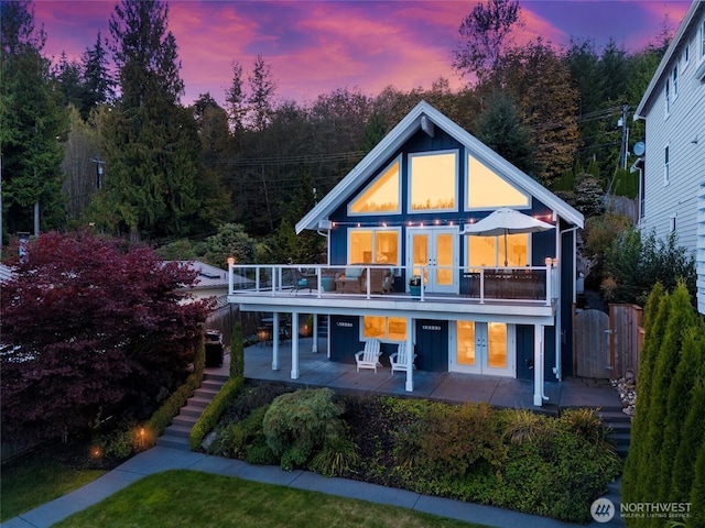 back of property at dusk with stairway, a gate, a patio area, french doors, and a deck