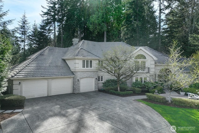 view of front of house with a garage, stucco siding, stone siding, a balcony, and concrete driveway