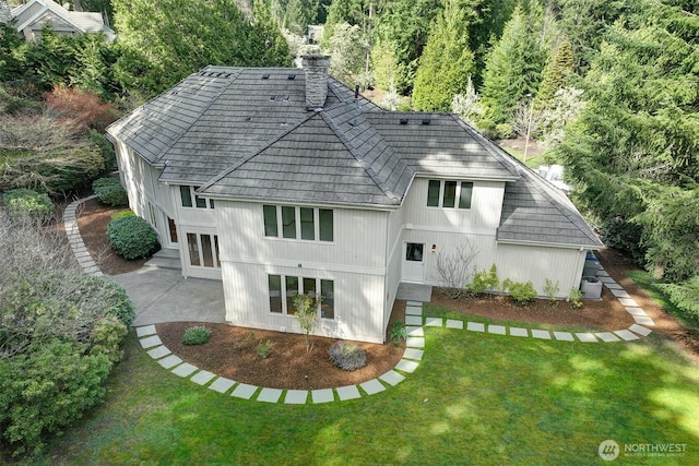 rear view of house with a chimney, a patio area, and a lawn