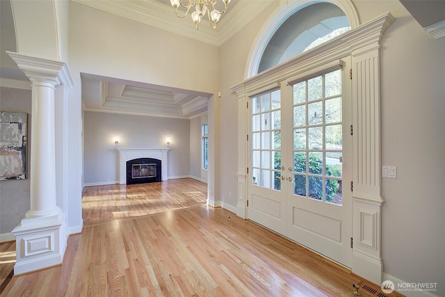 entryway with crown molding, light wood-style flooring, decorative columns, and a fireplace