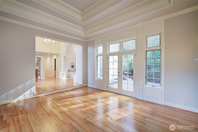 unfurnished room with a raised ceiling, arched walkways, light wood-style floors, crown molding, and ornate columns
