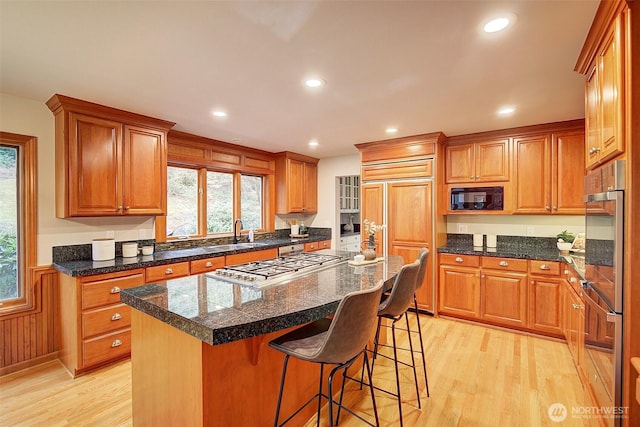 kitchen featuring a wainscoted wall, a center island, light wood finished floors, a breakfast bar area, and built in appliances