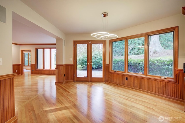 interior space featuring a chandelier, light wood-style floors, french doors, and a wainscoted wall