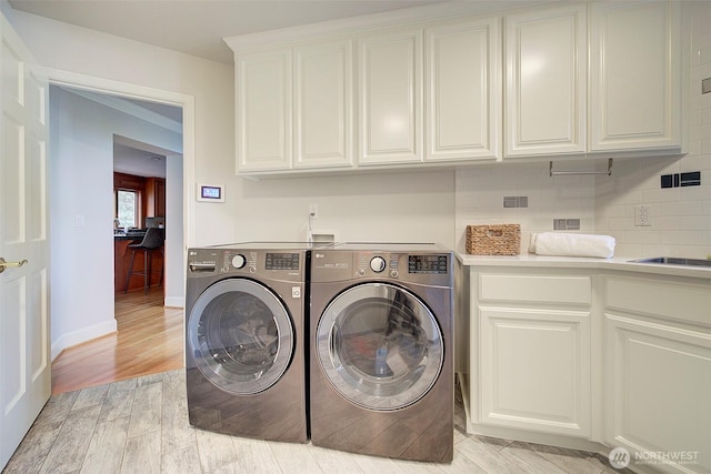 laundry area with separate washer and dryer, baseboards, cabinet space, light wood finished floors, and a sink