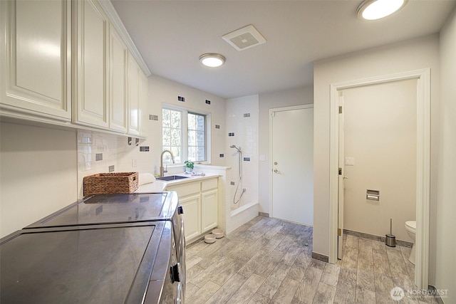 kitchen featuring tasteful backsplash, visible vents, washer and dryer, a sink, and light wood-style floors