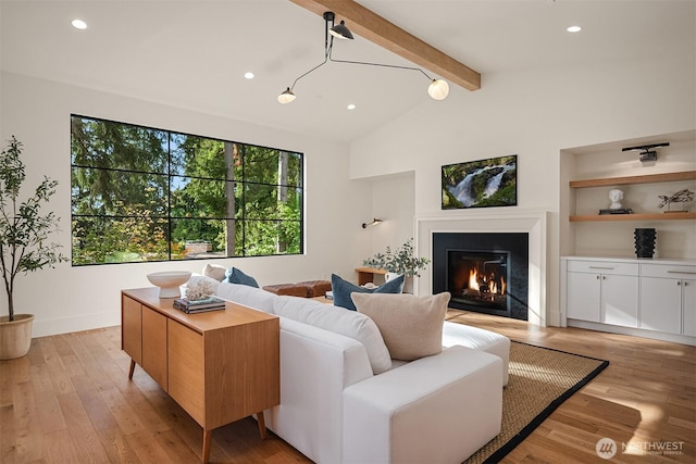 living room featuring recessed lighting, a lit fireplace, built in shelves, light wood-style flooring, and vaulted ceiling with beams