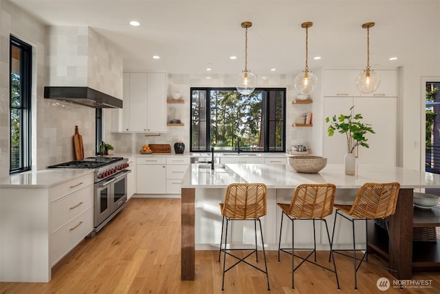 kitchen with light countertops, open shelves, double oven range, wall chimney exhaust hood, and light wood-style floors
