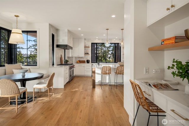 kitchen featuring white cabinetry, a breakfast bar area, high end stove, light wood finished floors, and wall chimney range hood