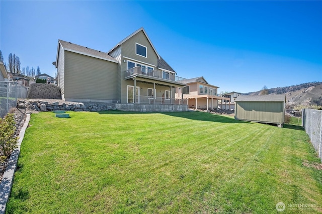 rear view of property featuring a storage shed, a yard, a fenced backyard, a balcony, and an outbuilding