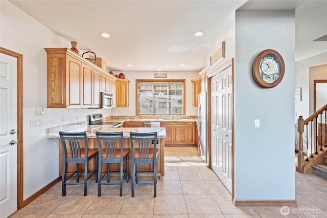 kitchen with light tile patterned floors, a peninsula, recessed lighting, a breakfast bar, and appliances with stainless steel finishes