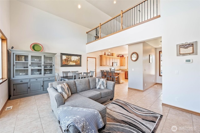 living room featuring a high ceiling, light tile patterned flooring, visible vents, and baseboards