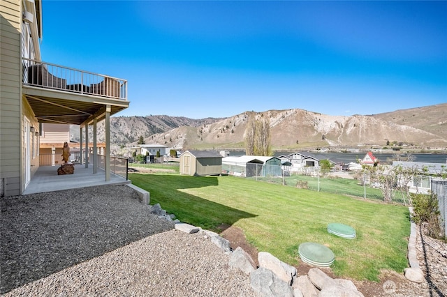 view of yard with a mountain view, fence, a patio, a storage unit, and an outbuilding