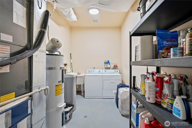 laundry room with water heater, heating unit, washer and clothes dryer, and laundry area