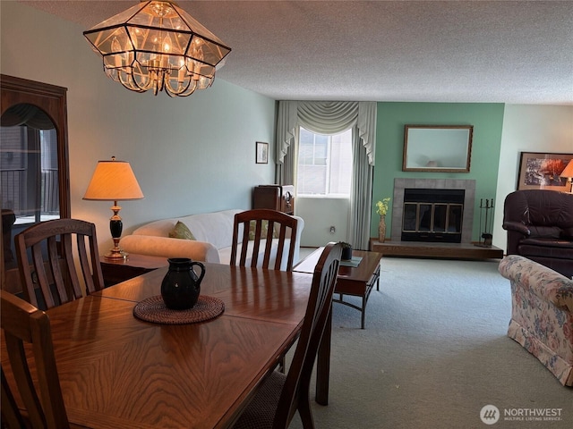 dining space with carpet, a textured ceiling, a chandelier, and a glass covered fireplace