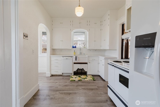 kitchen with white appliances, tasteful backsplash, arched walkways, a sink, and light wood-style floors