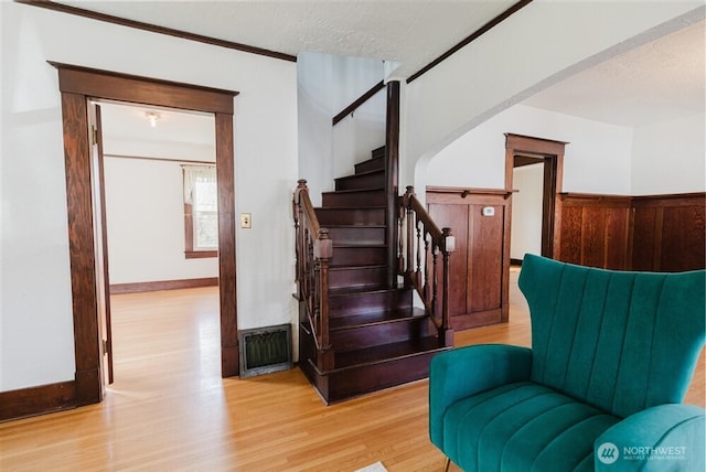 stairs featuring a textured ceiling, visible vents, wood finished floors, arched walkways, and wainscoting