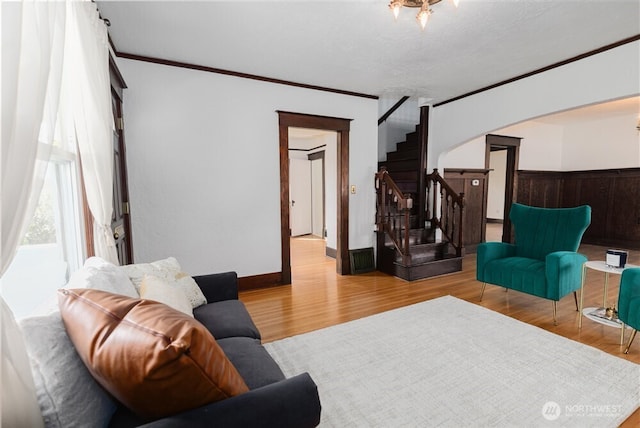 living room featuring ornamental molding, wood finished floors, stairway, arched walkways, and wainscoting