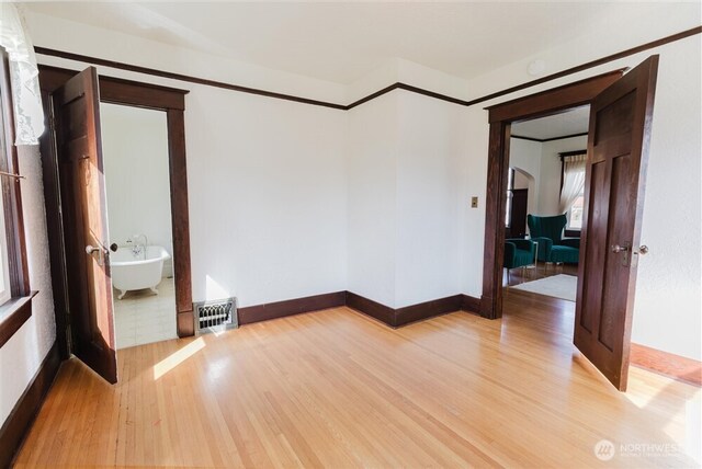 empty room featuring arched walkways, baseboards, light wood-style flooring, and visible vents