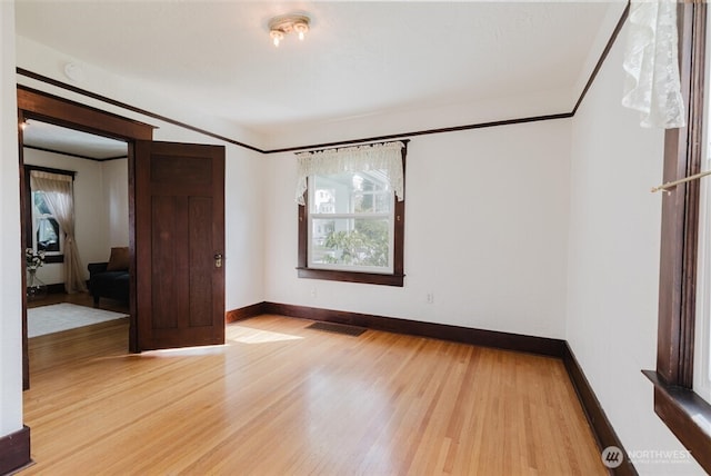 empty room featuring baseboards, ornamental molding, visible vents, and light wood-style floors