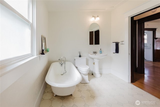 bathroom with baseboards, a freestanding bath, and toilet