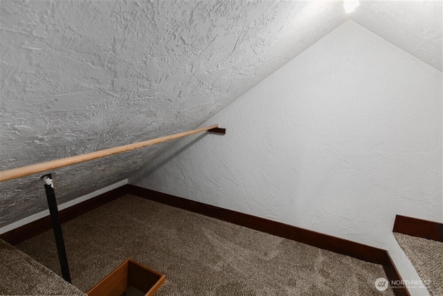 interior space featuring baseboards, carpet, a textured wall, and vaulted ceiling