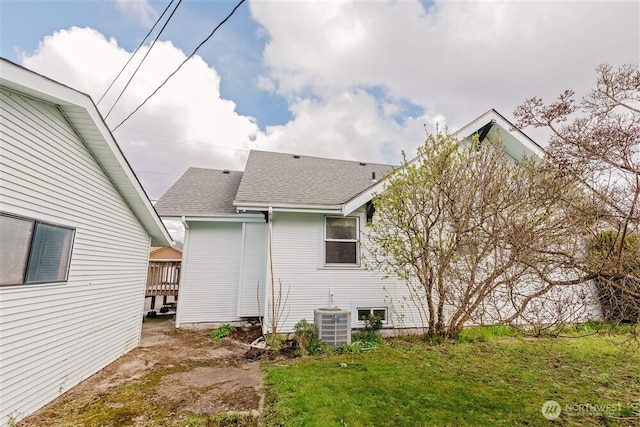 back of property with cooling unit, roof with shingles, and a lawn